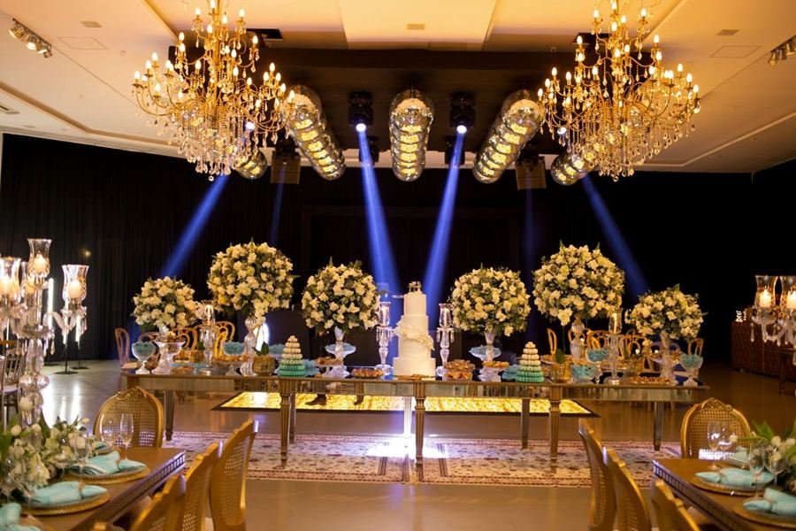 Salão de festa decorado, com a mesa do bolo e luz de palco.