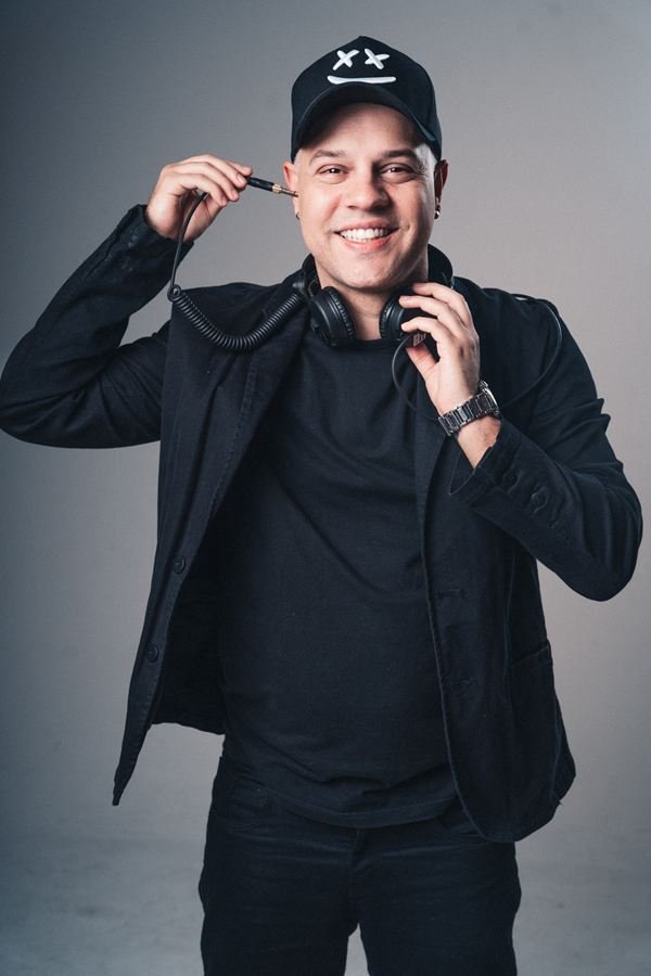 Edd Barros DJ de boné e jaqueta preta, com o fone no pescoço e o cabo na mão.